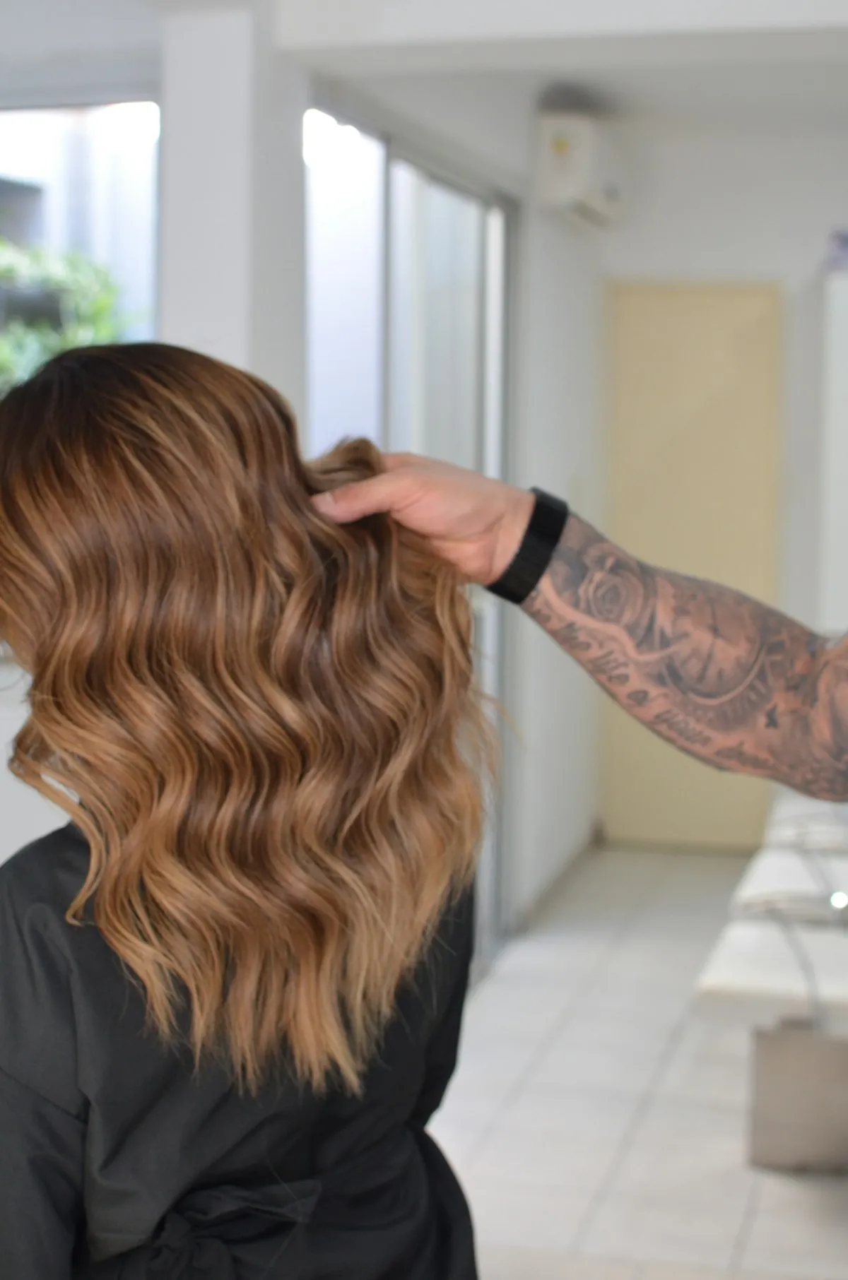 A stylist smoothing long caramel waves on a client in a bright salon