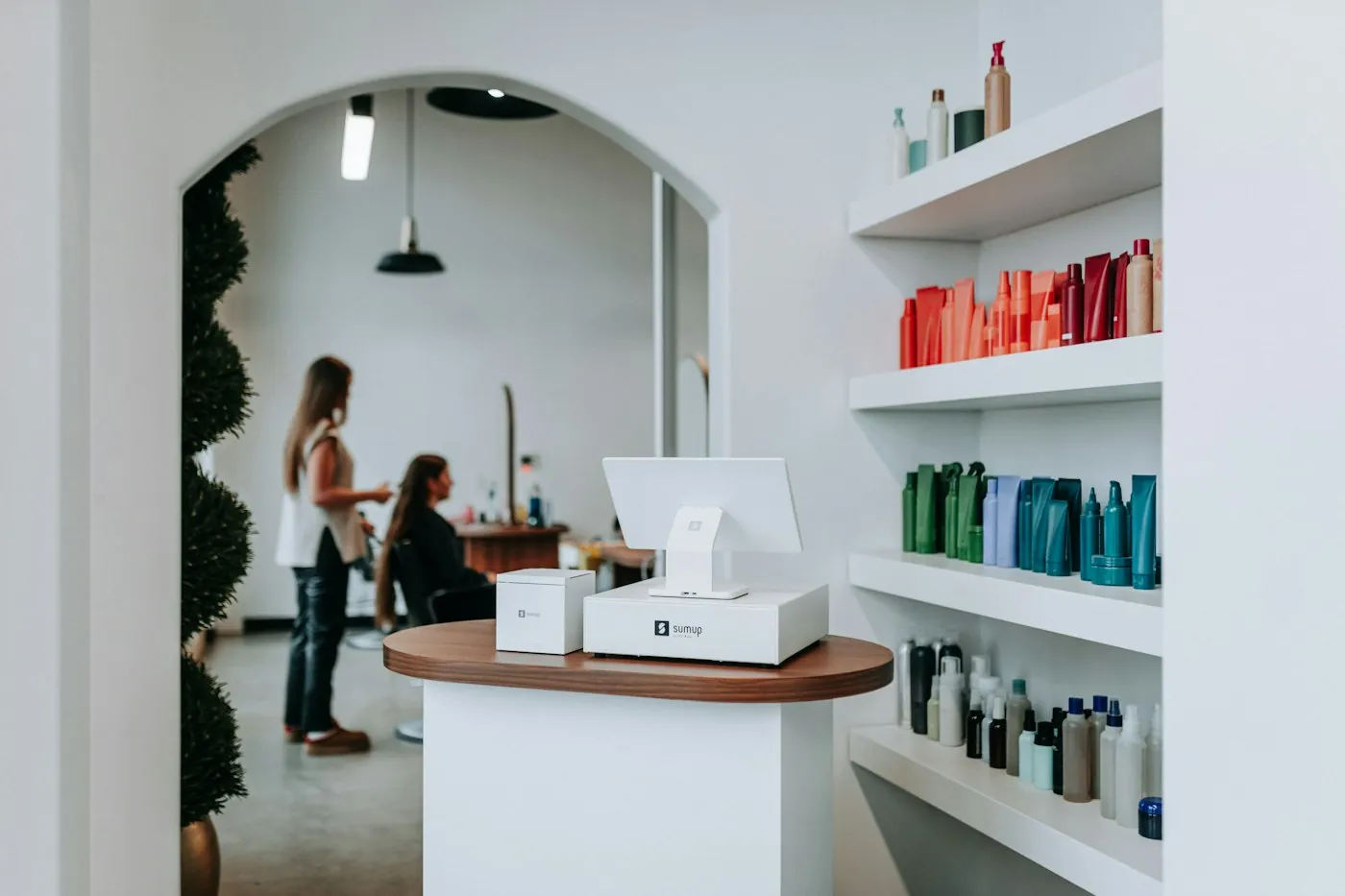 A bright salon with an arched doorway, plants and shelves of hair products