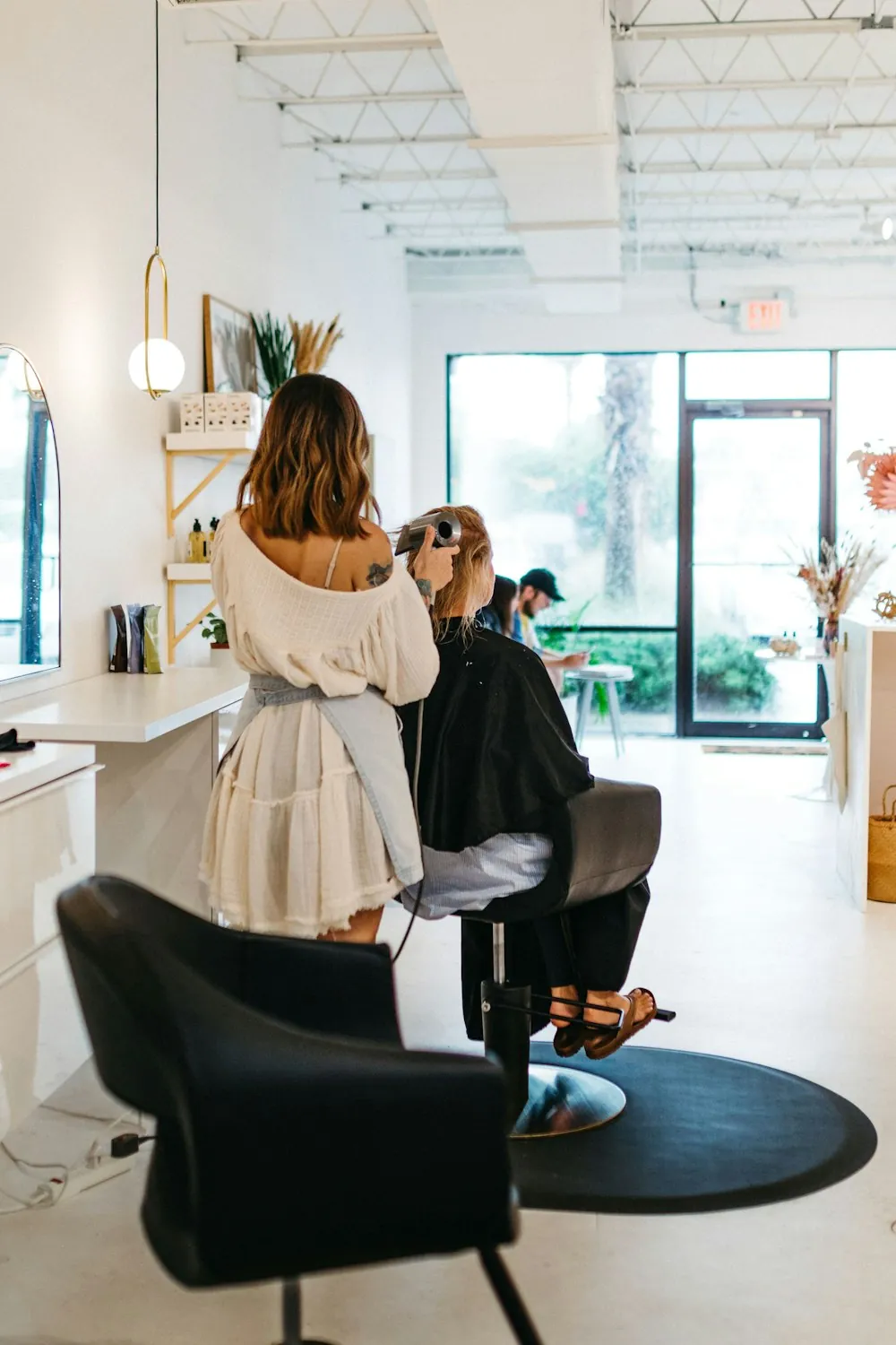 A stylist working with a client at a salon chair near the window
